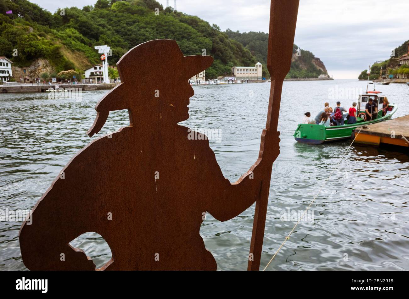 Pasajes, Gipuzkoa, Paesi Baschi, Spagna - 21 luglio 2019 : statua di Batelera (donna barca) e piccola barca a traghetto al molo sull'estuario di Oyarzun. Inc Foto Stock