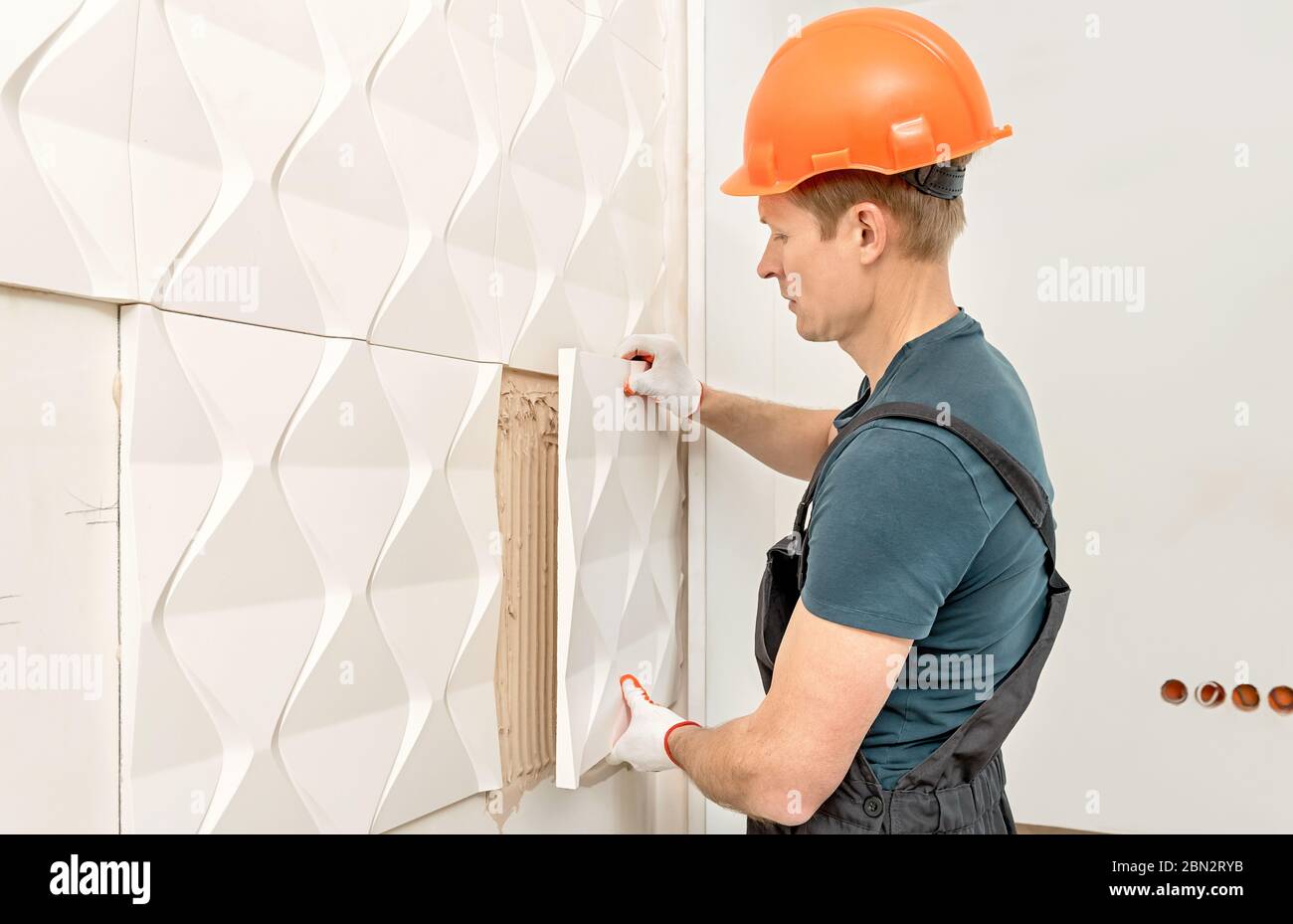 Installazione del pannello 3D in gesso. Il lavoratore sta attaccando la piastrella di gesso al muro. Foto Stock