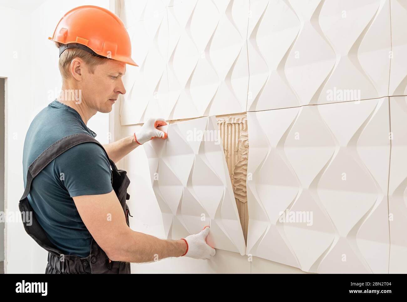 Installazione del pannello 3D in gesso. Il lavoratore sta attaccando la piastrella di gesso al muro. Foto Stock