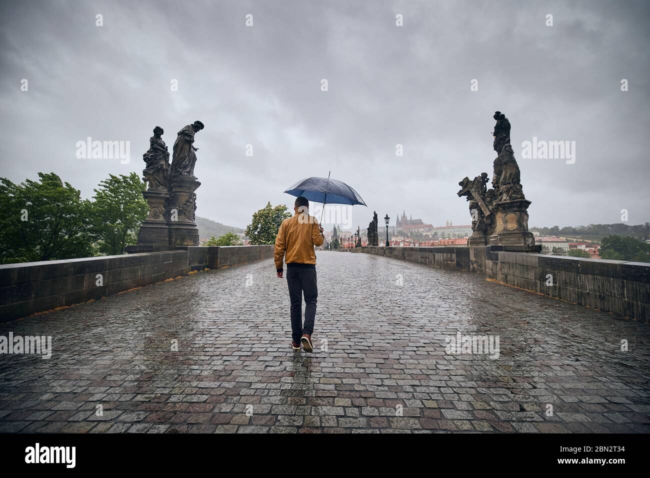 Uomo solitario con ombrello in forte pioggia camminando sul Ponte Carlo vuoto. Praga Repubblica Ceca Foto Stock