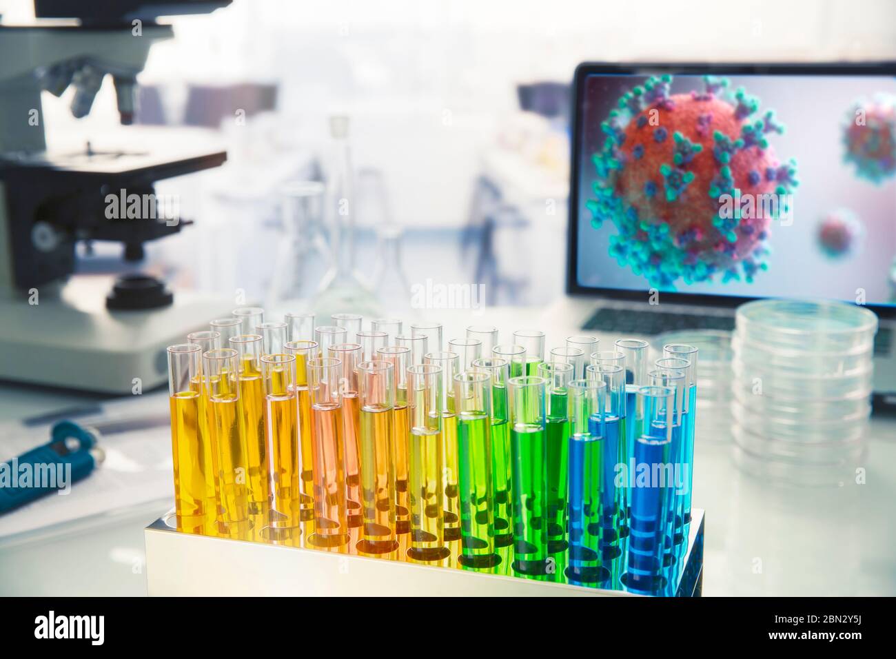 Fiale multicolore sul tavolo da laboratorio accanto al coronavirus sullo schermo Foto Stock
