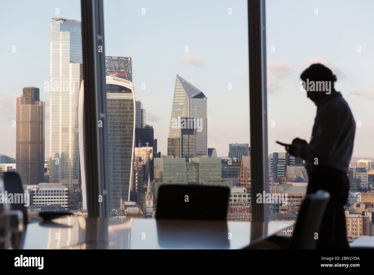 Silhouette uomo d'affari utilizzando smartphone alla finestra urbana alta Foto Stock