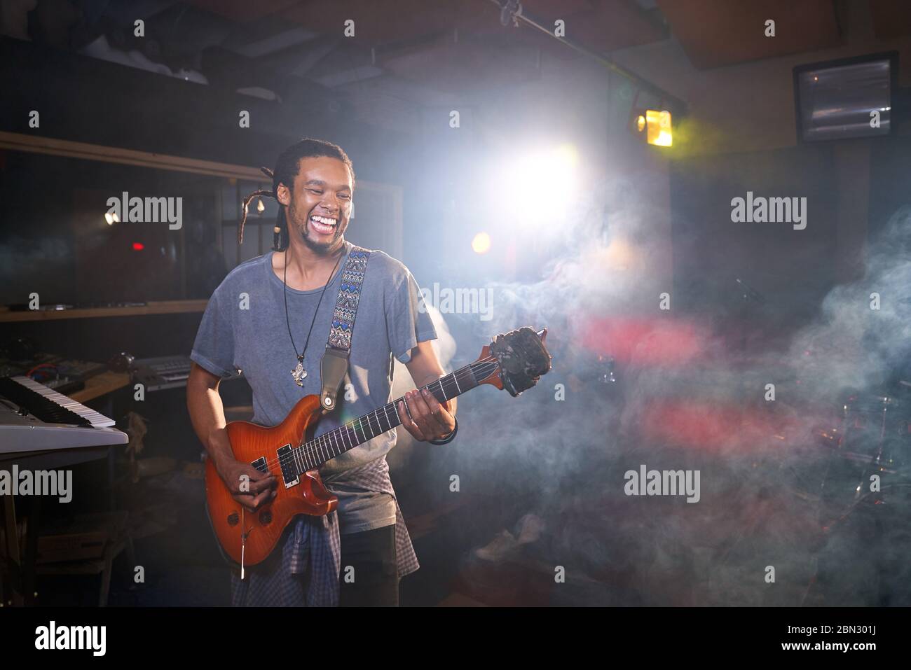 Un musicista maschio sorridente che suona la chitarra elettrica in studio di registrazione Foto Stock