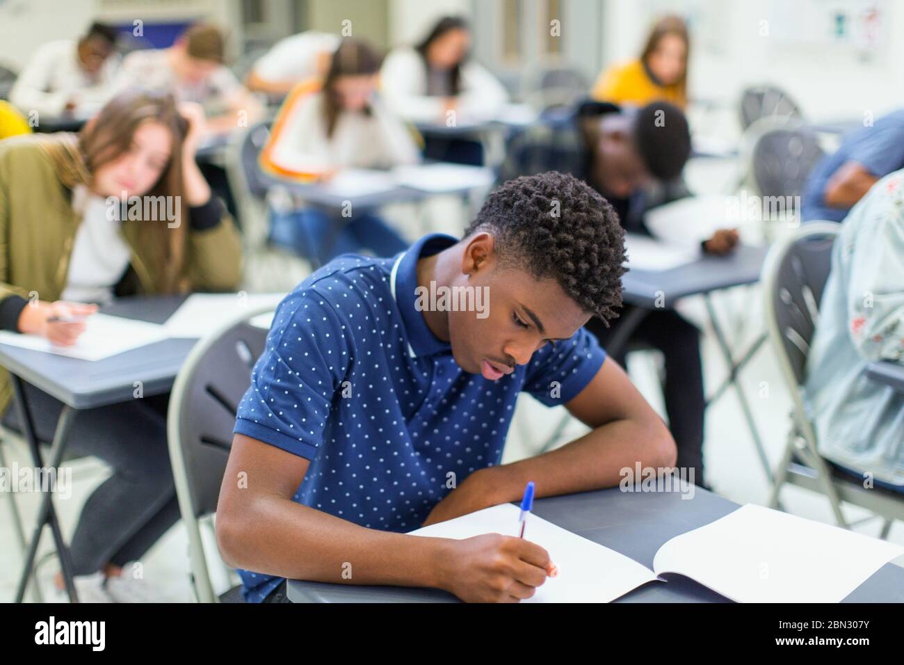 Studente di scuola superiore che si occupa di esami alla scrivania in classe Foto Stock