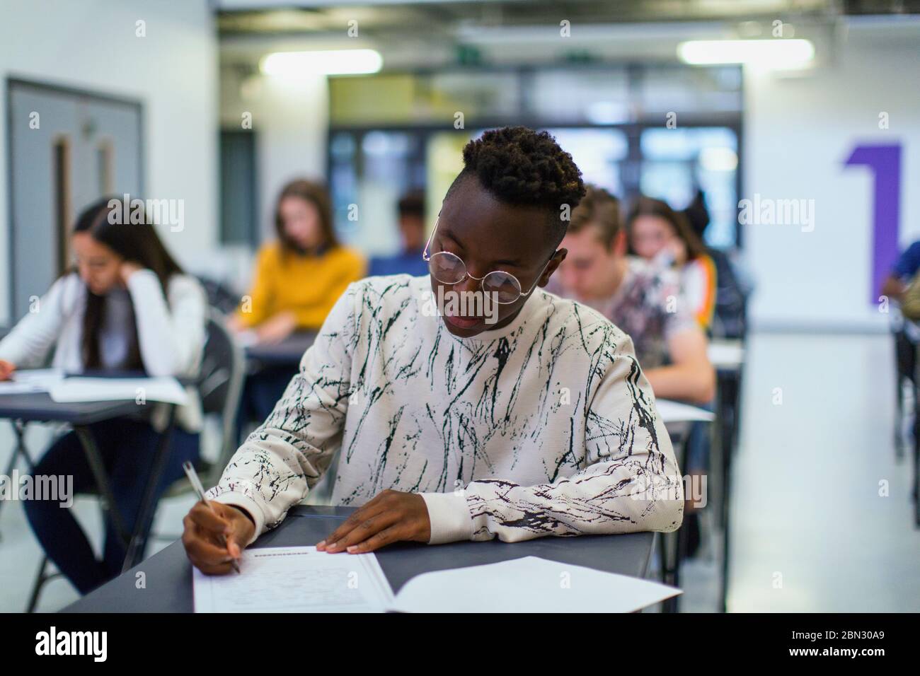 Studente di scuola superiore che si occupa di esami alla scrivania in classe Foto Stock