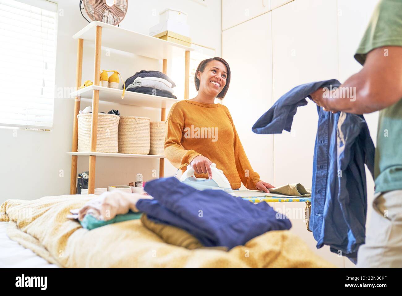 Donna felice che stira la lavanderia e che parla con il marito Foto Stock