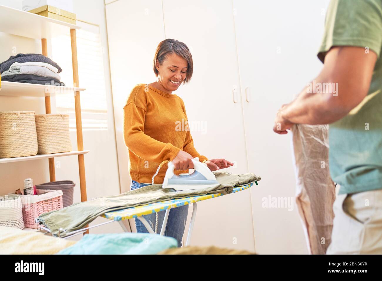 Donna sorridente che stira pantaloni a casa Foto Stock