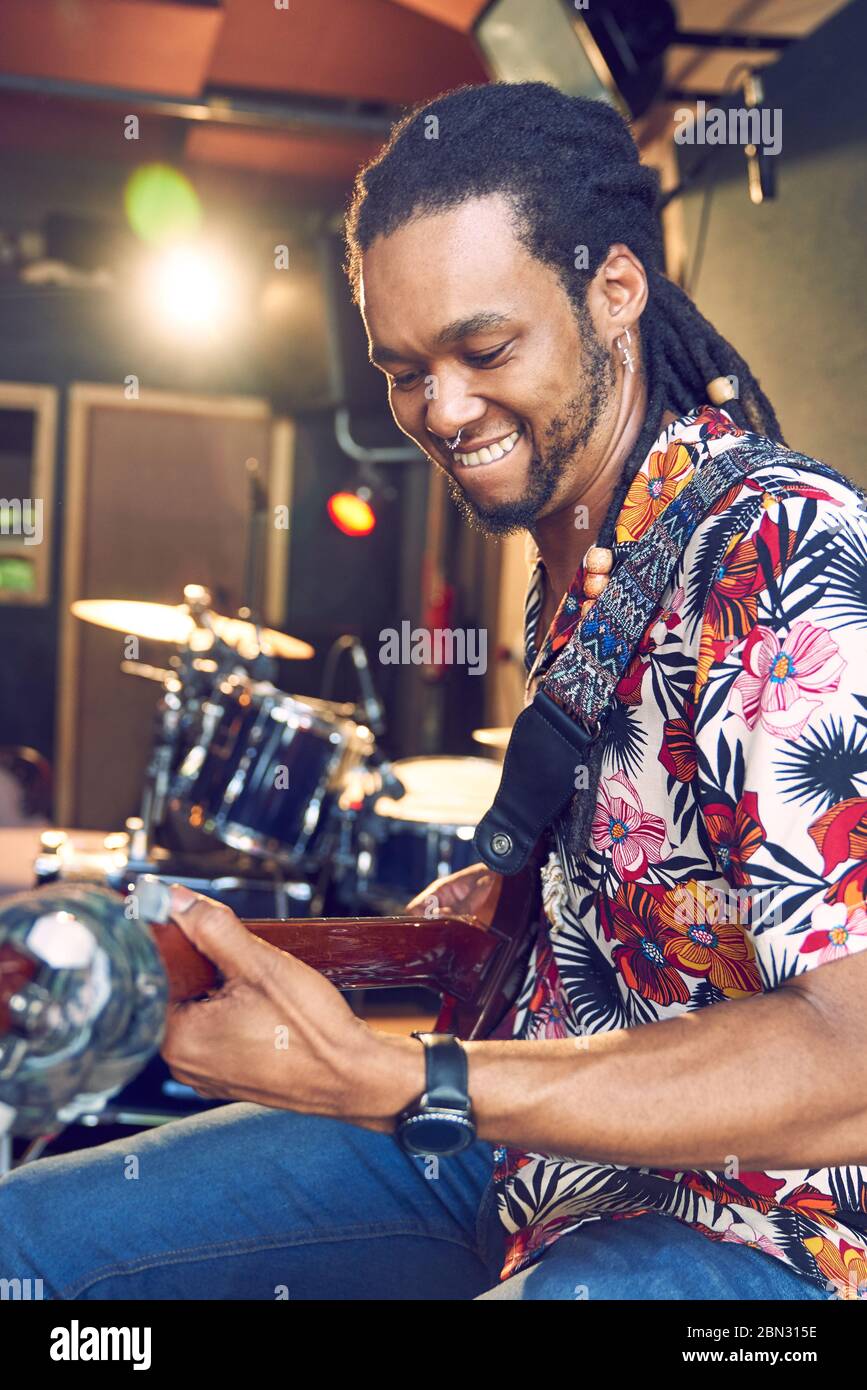 Un musicista maschio sorridente che suona la chitarra in studio di registrazione Foto Stock