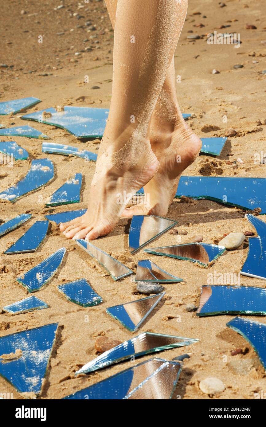 Gambe femminili e protezioni specchio sulla sabbia Foto Stock