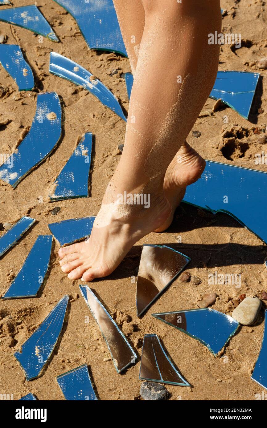 Gambe femminili e protezioni specchio sulla sabbia Foto Stock