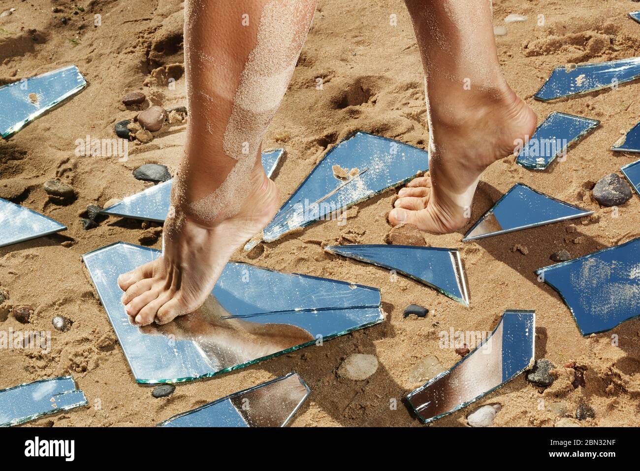 Gambe femminili e protezioni specchio sulla sabbia Foto Stock