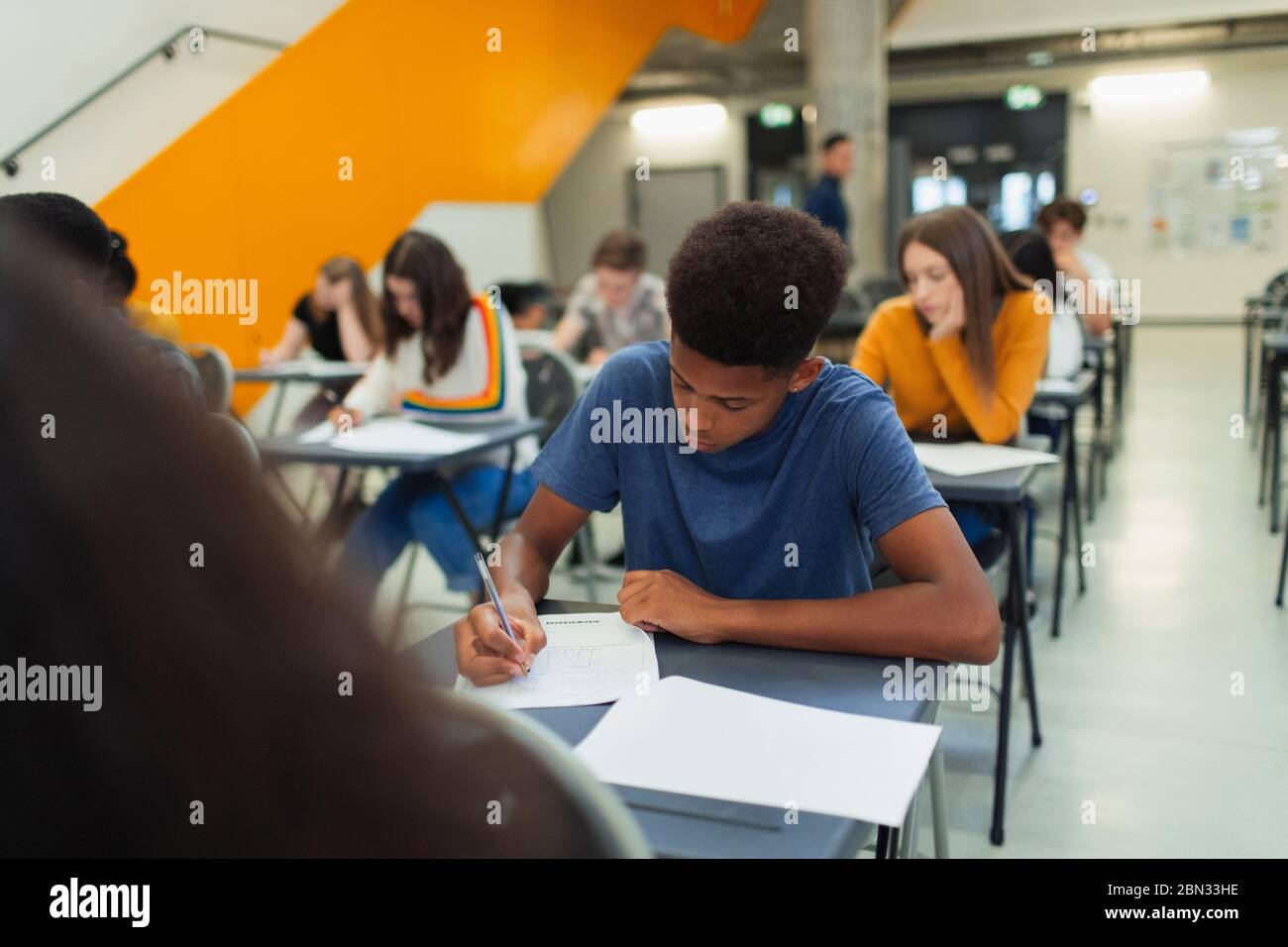 Studente di scuola superiore che si è messo a fuoco che sta prendendo l'esame alla scrivania Foto Stock