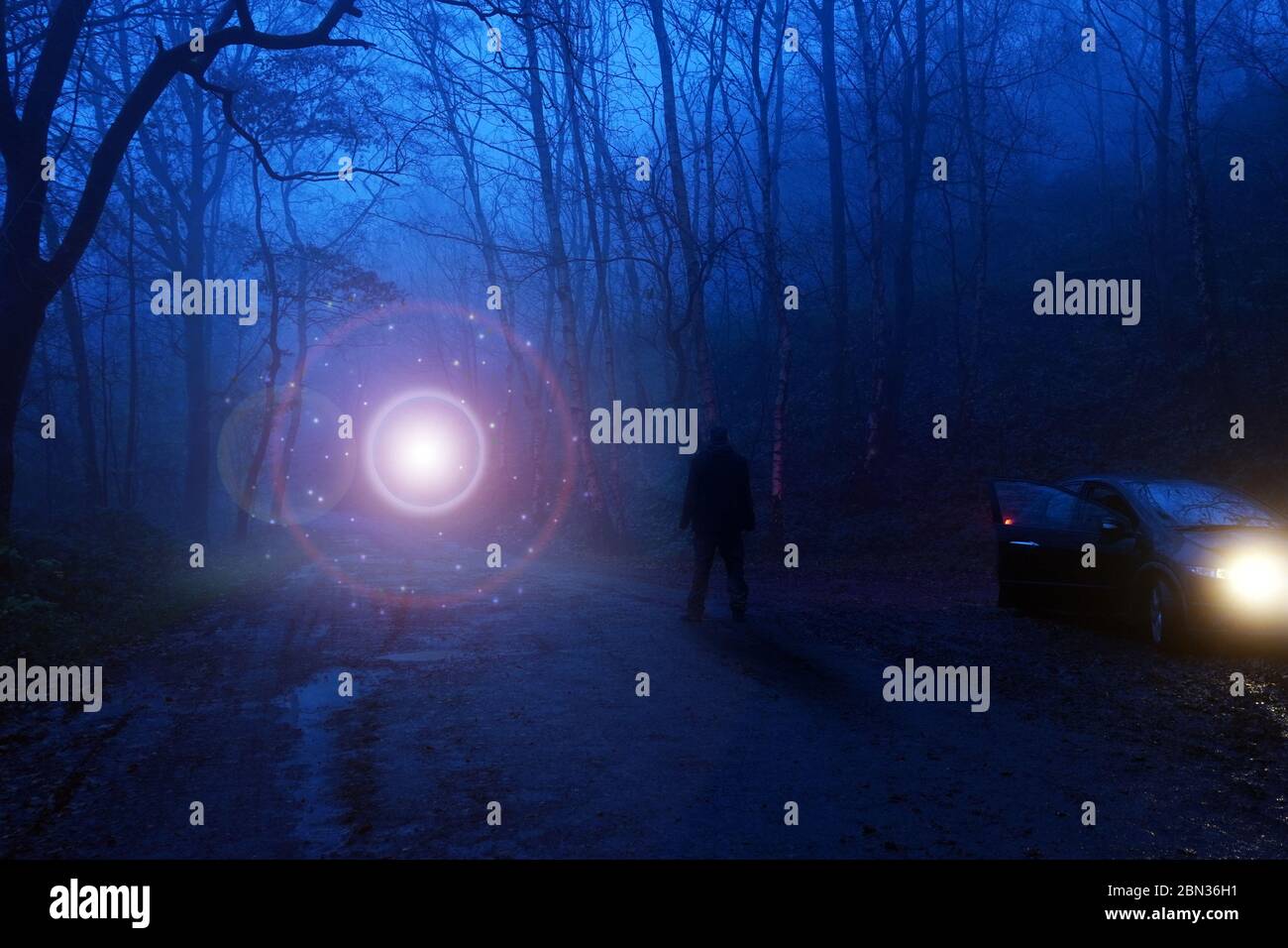 Un uomo accanto a un'auto che guarda un UFO luminoso, galleggiando sopra una pista in una foresta misteriosa e spettrale, concetto di fantascienza. Foto Stock