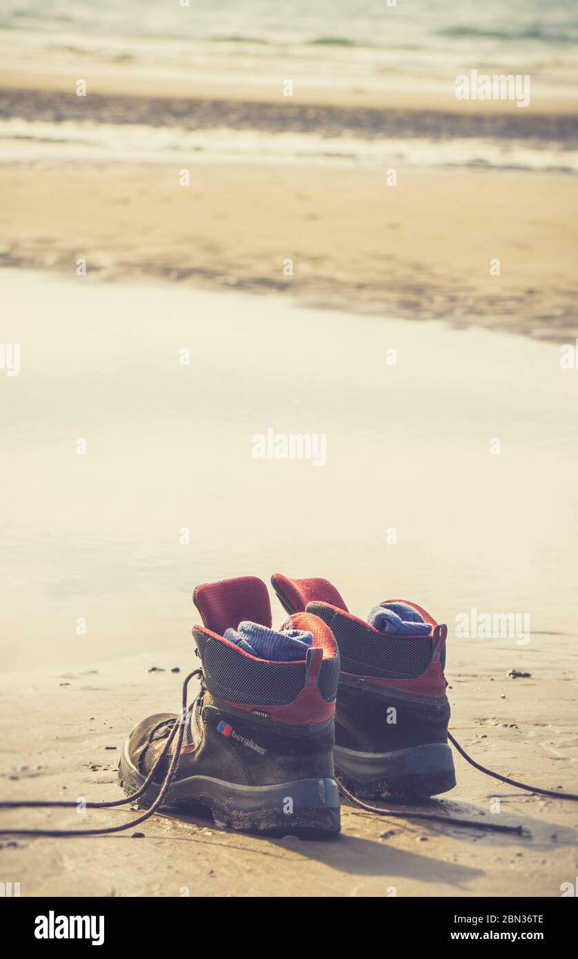 Primo piano di scarpe da passeggio e calze da uomo isolate sulla sabbia, a Newborough Beach, Anglesey, UK. Nessuna persona. Spazio di copia. Foto Stock