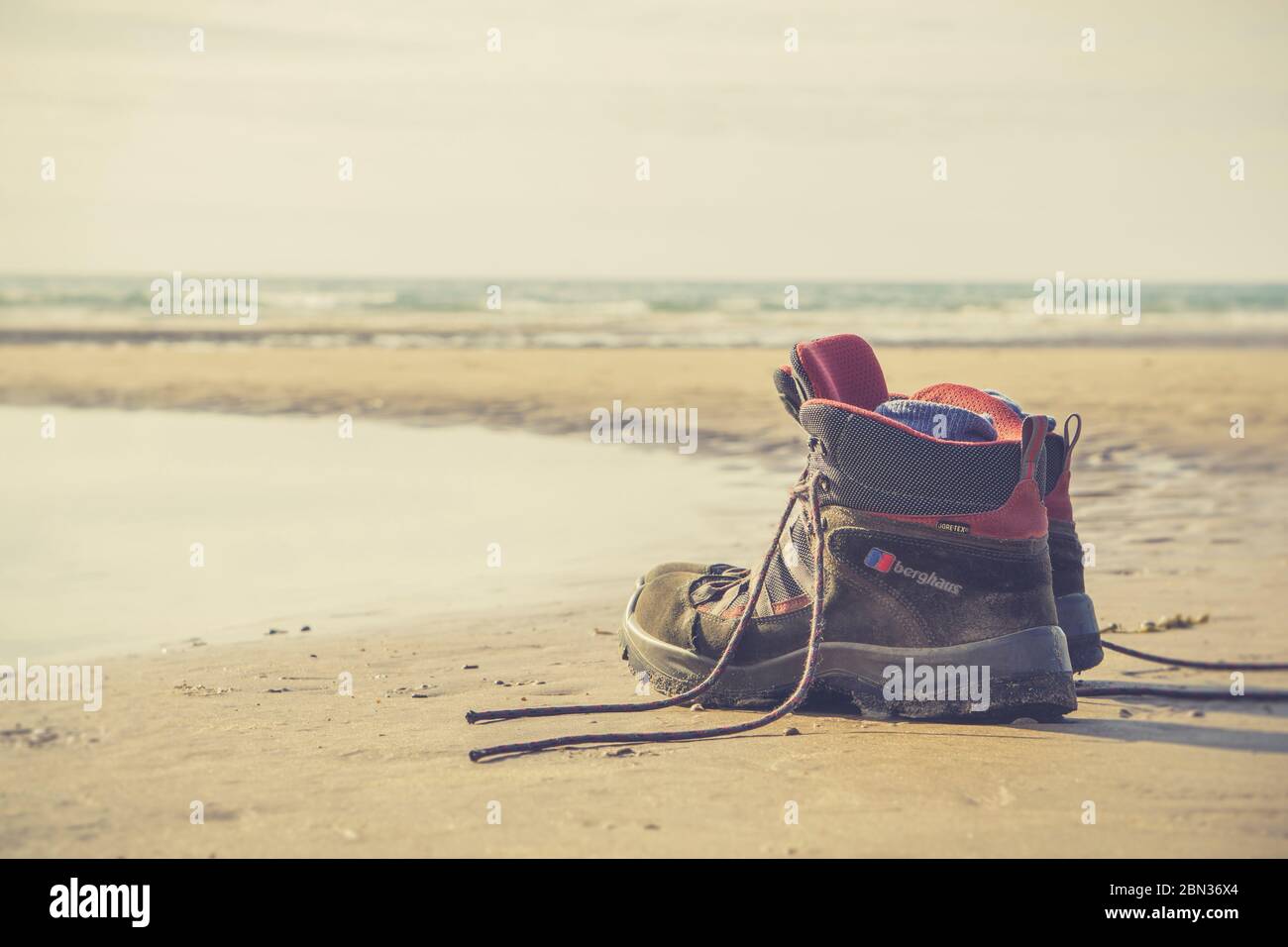 Primo piano di scarpe da passeggio e calze da uomo isolate sulla sabbia, a Newborough Beach, Anglesey, UK. Nessuna persona. Spazio di copia. Foto Stock