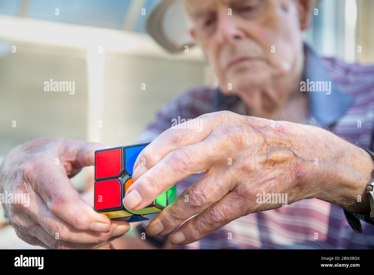 Closeup di un uomo anziano che usa un puzzle tipo cubo Rubix come terapia per la sua capacità mentale diminuita a causa di lesioni alla testa e danni cerebrali causati da un Foto Stock