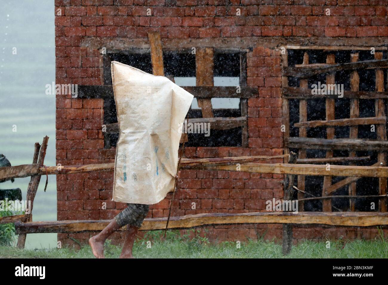 Uomo che si ripara sotto un sacchetto di plastica in forte pioggia. Madagascar. Foto Stock