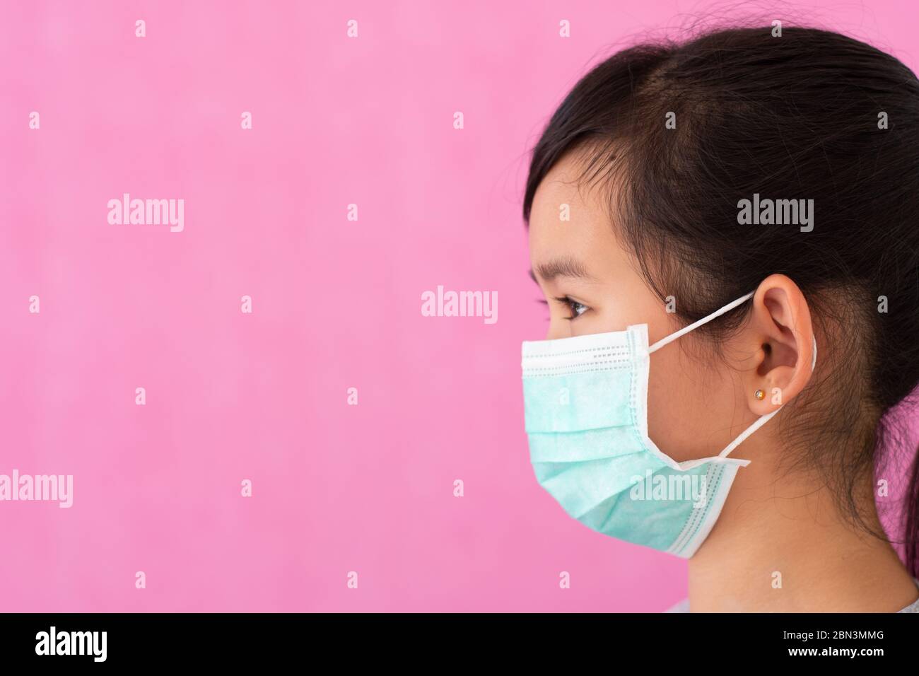 Bambina asiatica che indossa una maschera medica sterile per proteggere Covid-19 isolato su sfondo rosa. Spazio di copia. Foto Stock