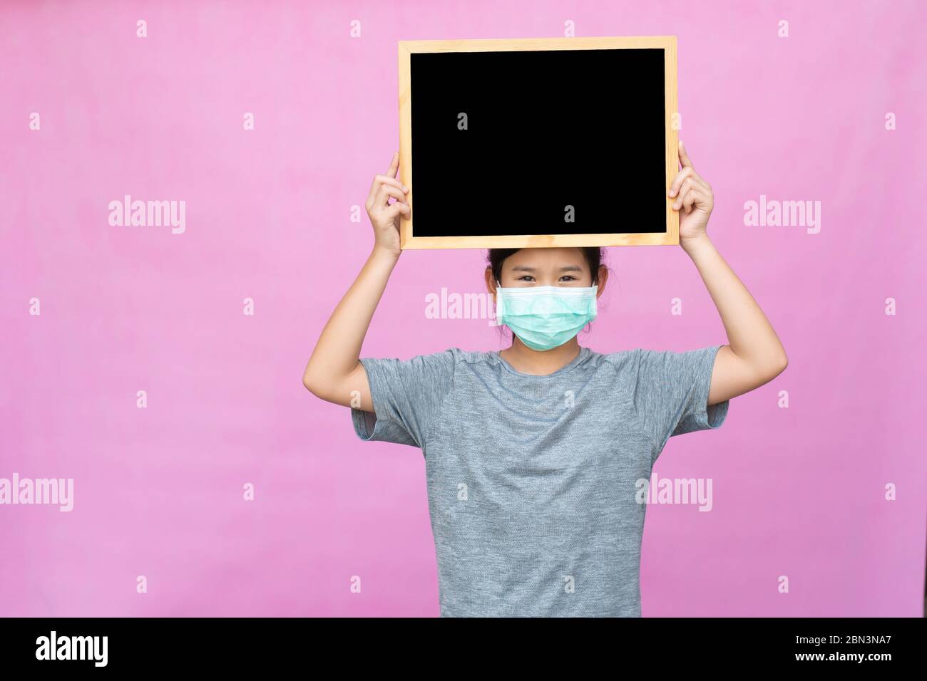 Piccola ragazza asiatica che tiene lavagna isolata su sfondo rosa. Foto Stock