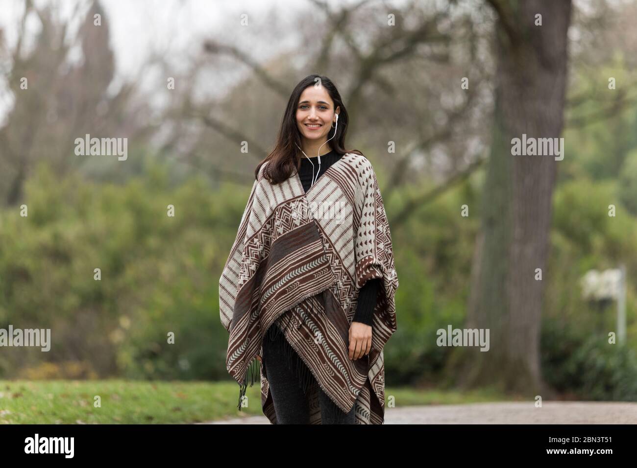 Bella donna indiana che indossa poncho e sorridente ampiamente nel parco. Foto Stock