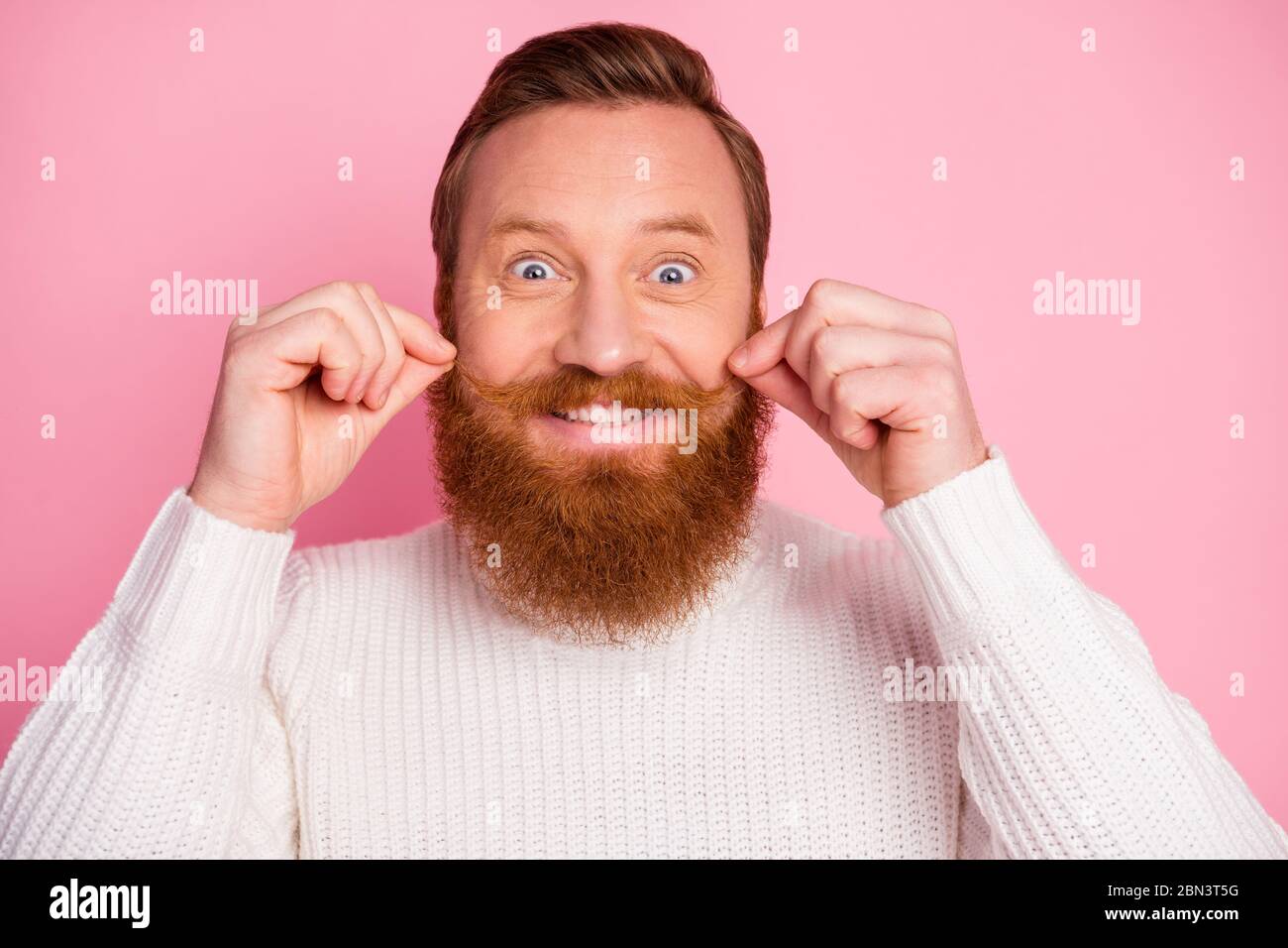 Primo piano del suo bel divertente comico allegro ragazzo rosso allegro che tocca baffi isolato su sfondo rosa colore pastello Foto Stock