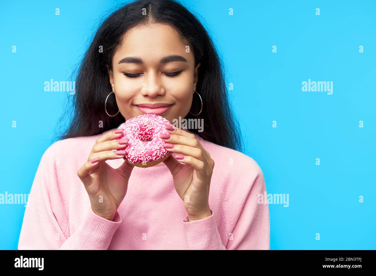 Cibo di tentazione. Bella donna nera godere donut isolato su sfondo blu. Foto Stock