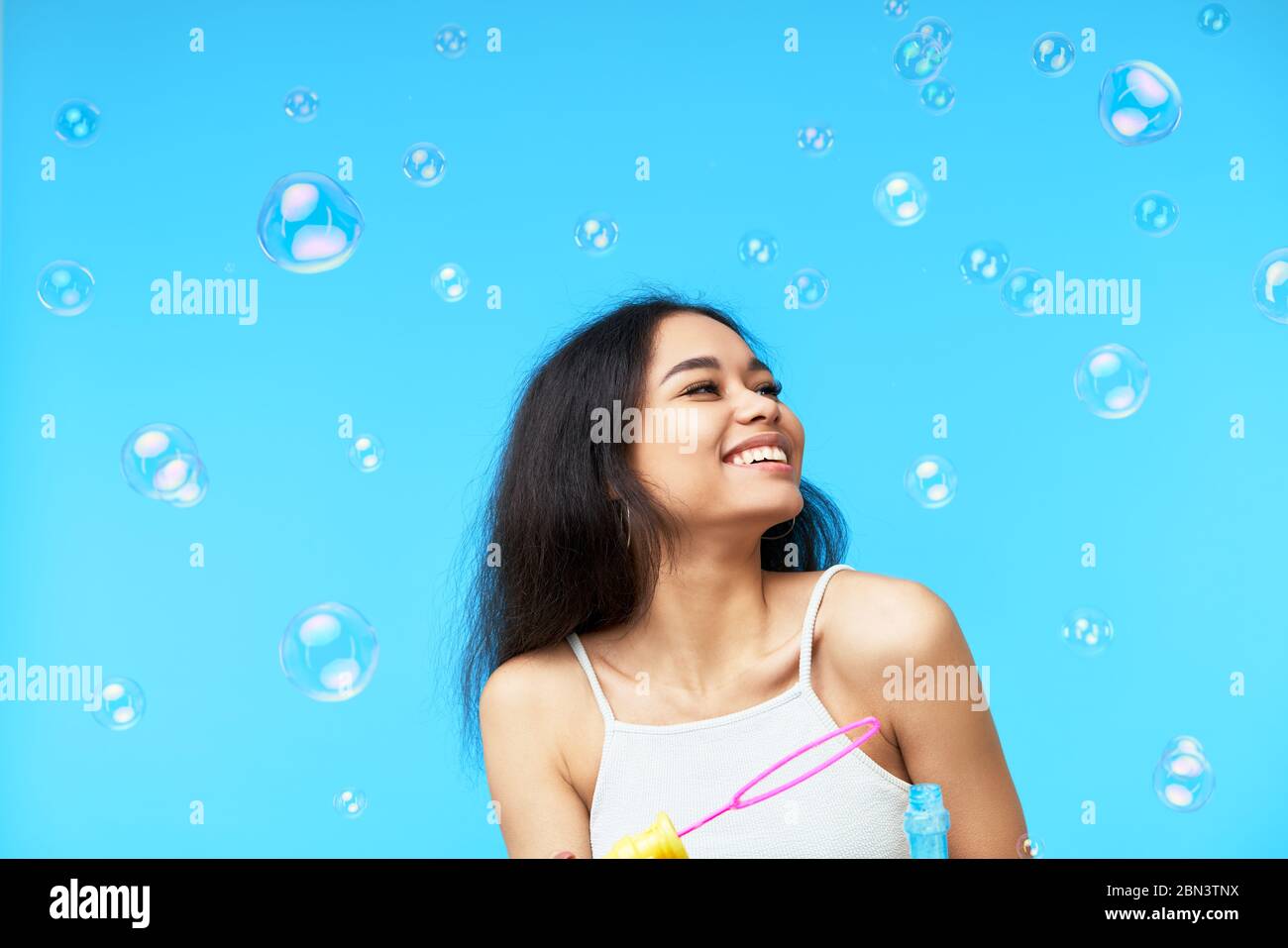 Felice donna nera sorridente godere di bolle di sapone su sfondo blu Foto Stock