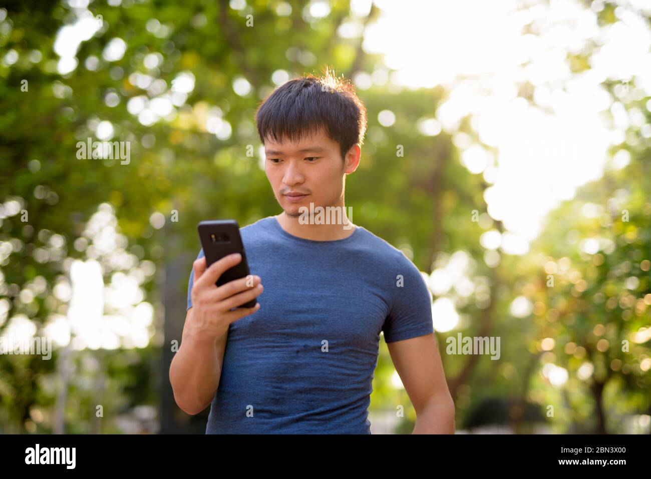 Ritratto di giovane asiatico utilizzando il telefono al parco all'aperto Foto Stock
