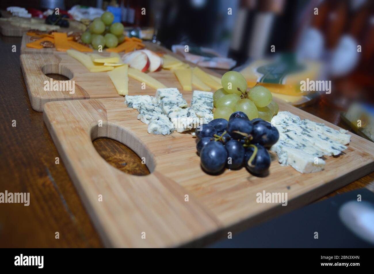 Primo piano di formaggio brie a muffa blu con uve su un piatto di legno con vari altri formaggi e frutta sullo sfondo preparato per un formaggio t Foto Stock