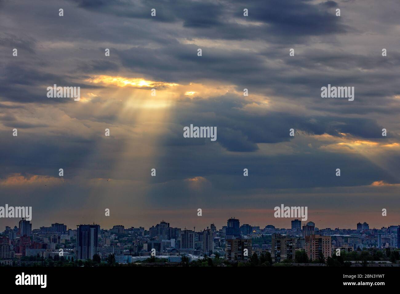 I raggi del sole si infrangono attraverso le dense nuvole all'alba su una città addormentata. Luce brillante nel suggestivo cielo mattutino. Foto Stock