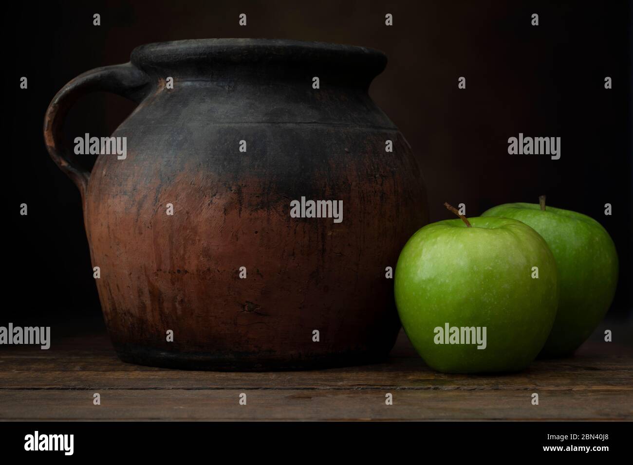 Due mele granny smith con vecchia brocca di ceramica. Scatto a livello degli occhi con un'atmosfera rustica scura. Foto Stock