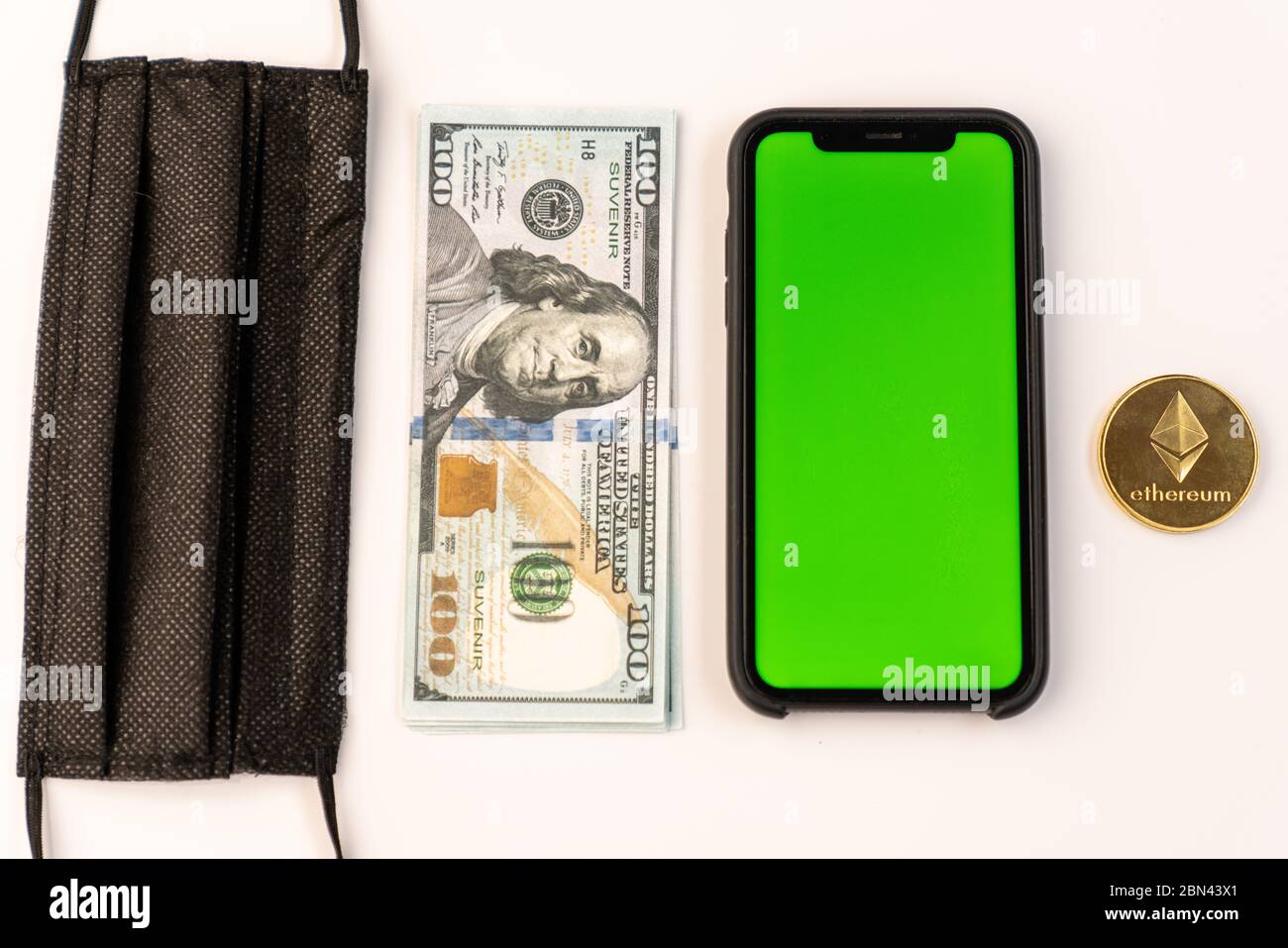 Primo piano di una maschera protettiva nera, bolletta del dollaro, telefono con schermo verde e moneta etereo isolato su bianco Foto Stock