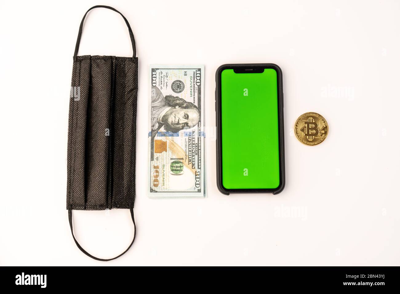 Vista dall'alto di una maschera protettiva nera, di una bolletta del dollaro, di un telefono con schermo verde e di una moneta dorata di bitcoin isolata su bianco Foto Stock