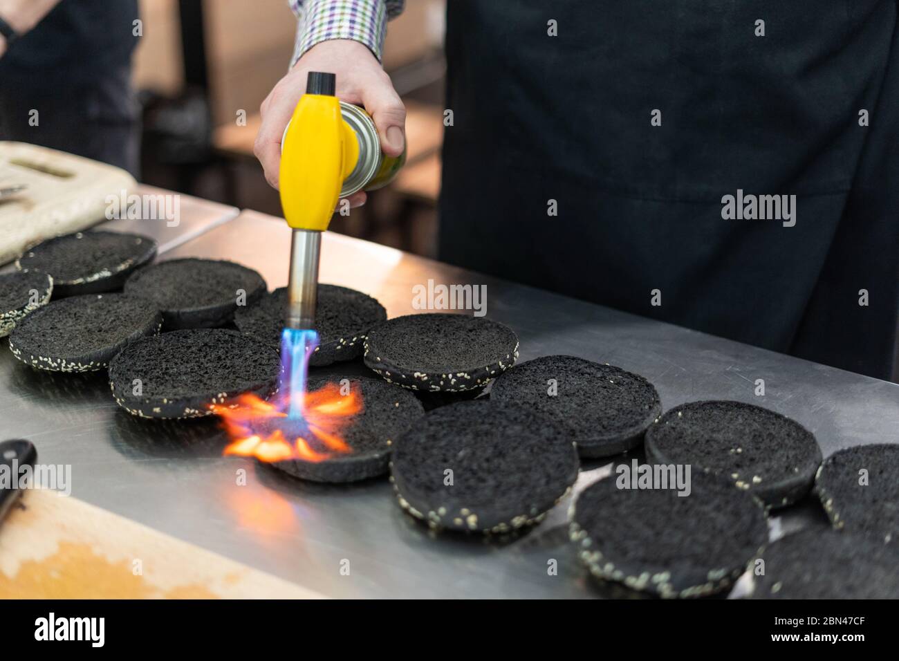 Uomo che elabora panini neri con una torcia da cucina Foto Stock