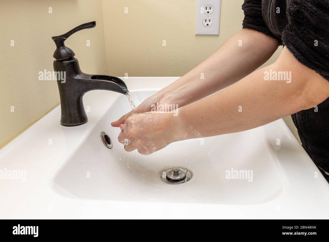 Donna lavando le mani con sapone e maniche arrotolate Foto Stock
