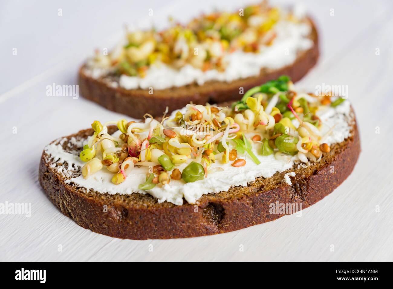 Colazione macrobiotica sana. Sandwich con formaggio cremoso, verdure microgreine di piselli e fagioli germogliati, noce, girasole e lino su sfondo ligneo. Foto Stock