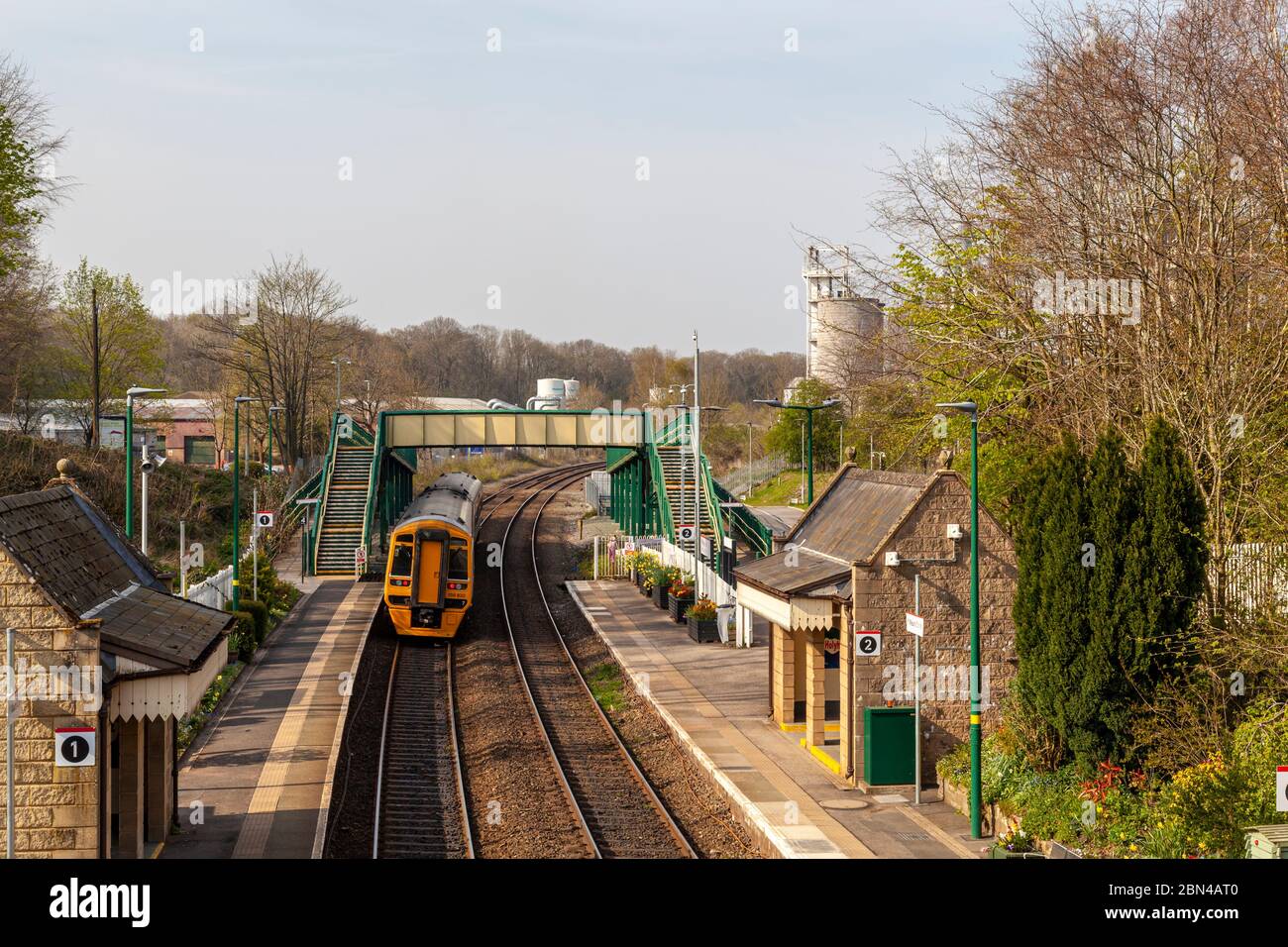 Un treno passeggeri parte dalla stazione ferroviaria di Chirk, con una parte dello stabilimento di Kronospan sullo sfondo, il Galles del Nord-Est Foto Stock