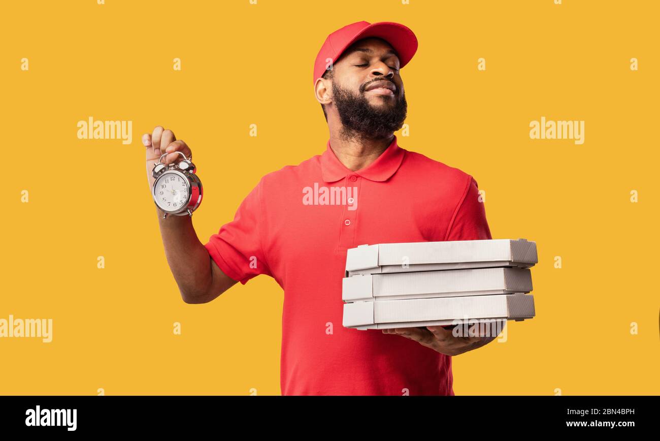Corriere consegna Pizza Holding scatole e orologio su sfondo giallo Foto Stock