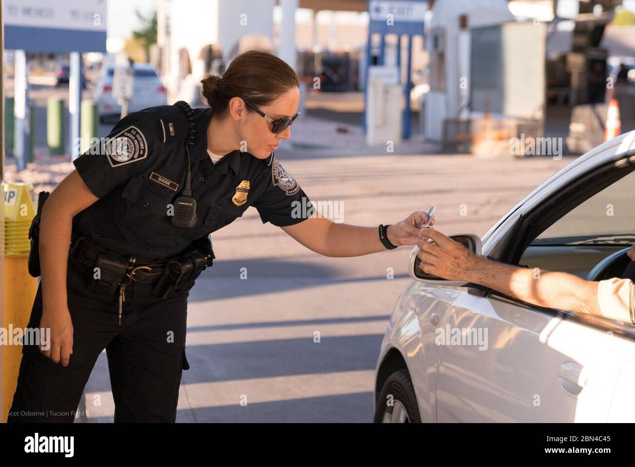 Un funzionario delle dogane e della protezione delle frontiere degli Stati Uniti dell'Office of Field Operations elabora un passeggero e ispeziona il veicolo prima di consentire l'ingresso negli Stati Uniti dal Messico al valico di frontiera di San Luis. Foto Stock