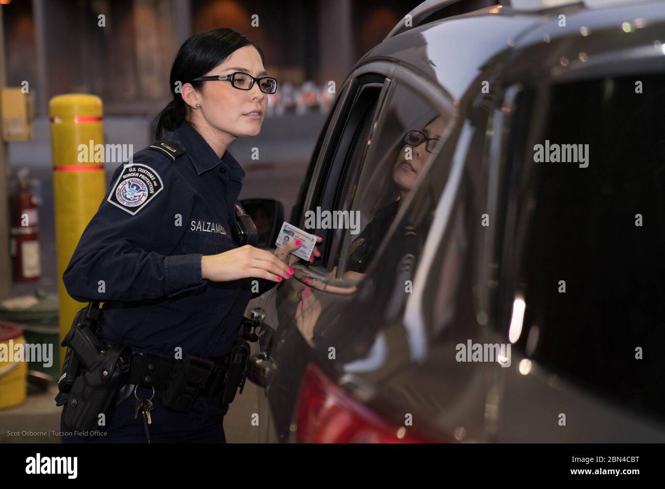 Un funzionario delle dogane e della protezione di frontiera degli Stati Uniti elabora un passeggero e ispeziona un veicolo al valico di frontiera di San Luis tra gli Stati Uniti e il Messico. Il funzionario verifica i dati di identificazione e del veicolo prima di entrare negli Stati Uniti Foto Stock