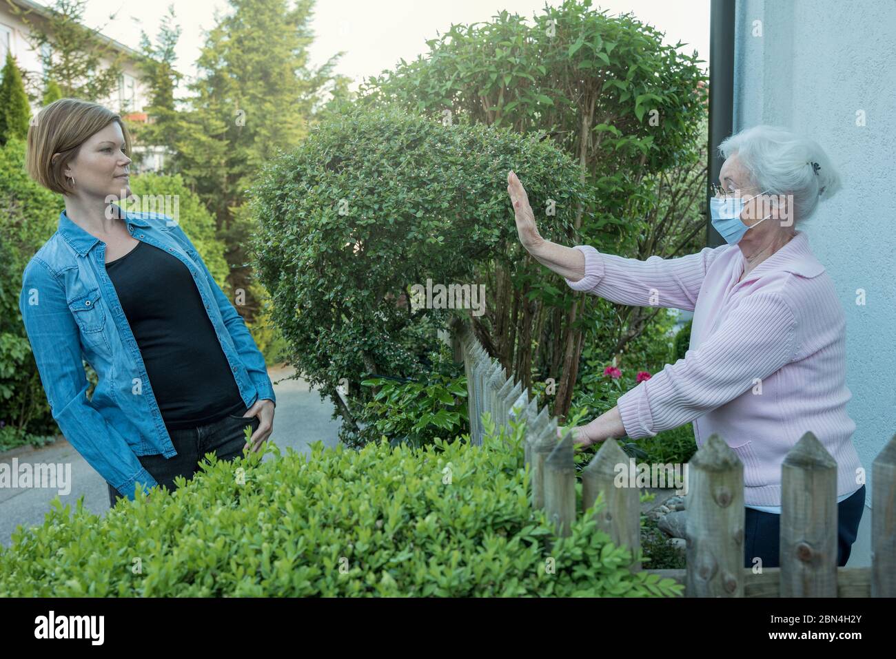Donna anziana con maschera facciale mostra la distanza di sicurezza verso la donna vicina Foto Stock