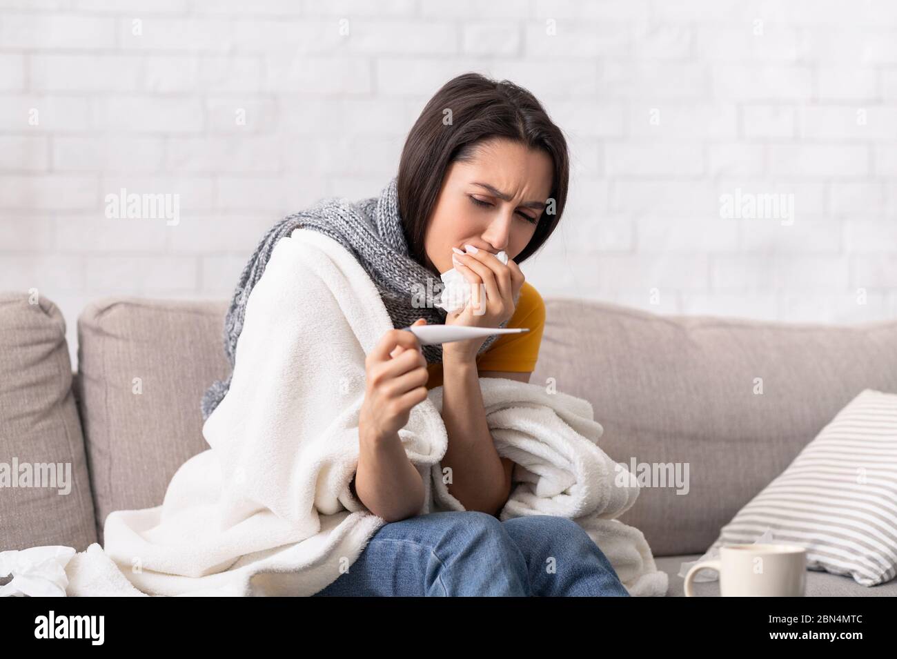Donna malata che soffre di cattiva infezione con febbre alta, guardando il termometro a casa Foto Stock