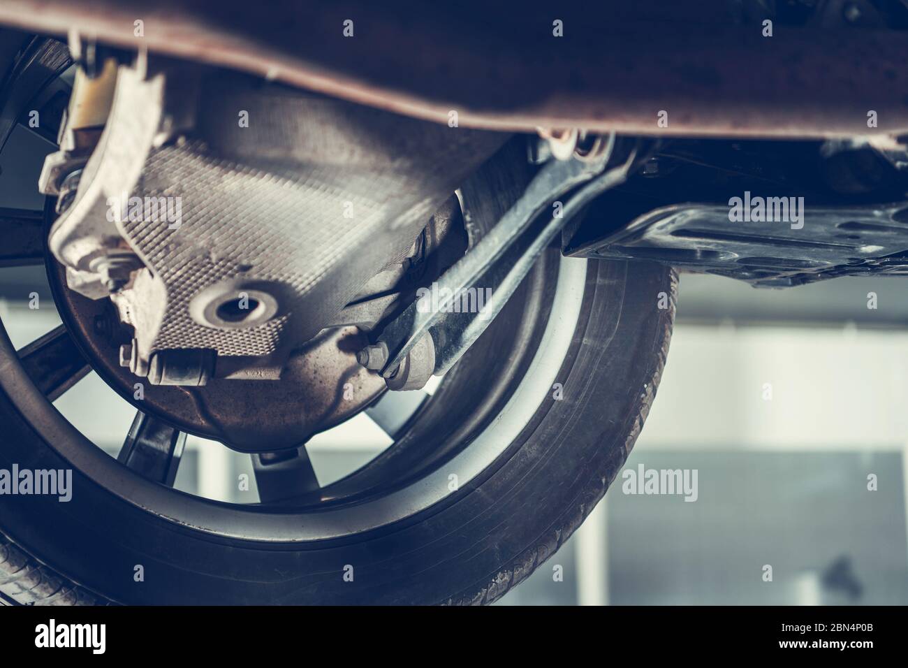 Primo piano del pneumatico e della parte inferiore della vettura sospesa sul sollevatore idraulico in manutenzione meccanica. Foto Stock