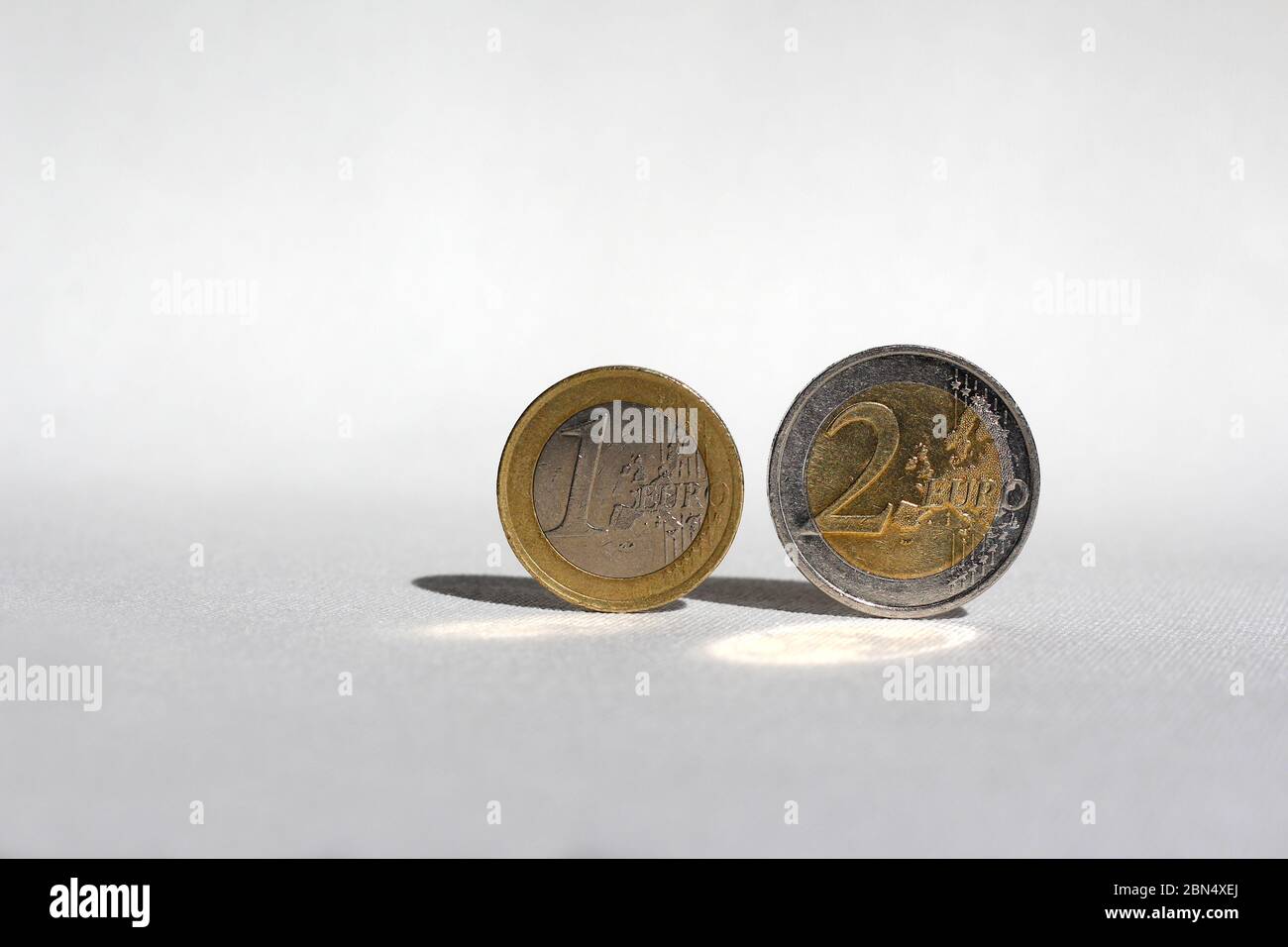 Euro monete bilanciamento senza alcun aiuto su una superficie bianca, la luce del sole crea riflessione e ombra Foto Stock