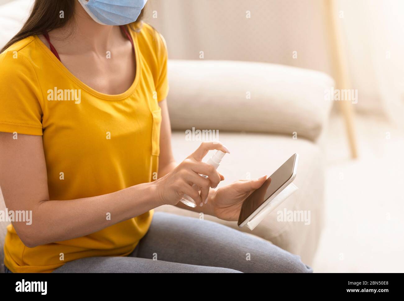 Donna irriconoscibile in maschera protettiva pulizia smartphone con antisettico al chiuso, primo piano. Spazio di copia Foto Stock