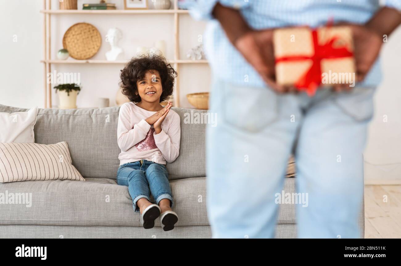 Festa. Uomo africano americano maturo che tiene presente per la sua nipote dietro la sua schiena in casa Foto Stock