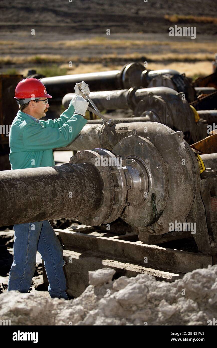 Un lavoratore che esamina e regola un corpo pompa in un impianto di produzione industriale. Foto Stock