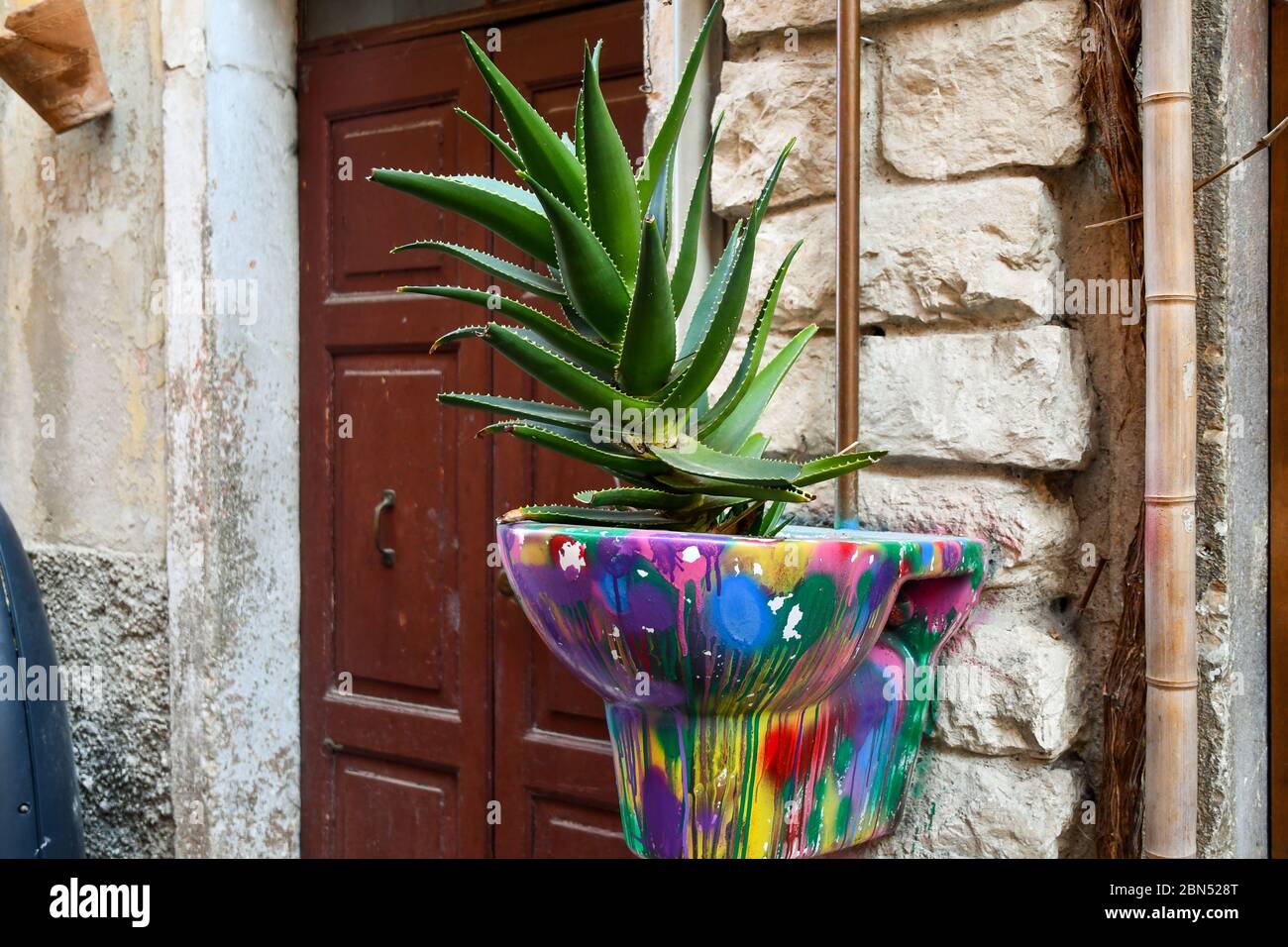 Primo piano di un'antica acqua dipinta appesa alla parete esterna di una casa e riutilizzata come pentola per piante, Garda, Verona, Veneto, Italia Foto Stock