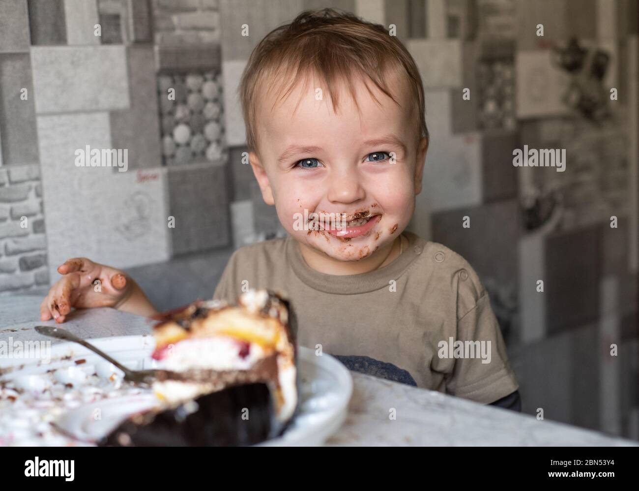 Il bambino mangia una torta e mostra emozioni. Il bambino si sporca in un dolce dessert. Ritratto bambino. Foto Stock