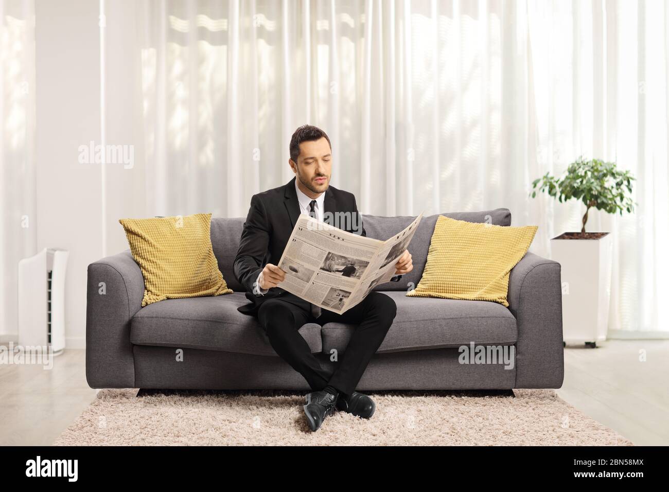 Ritratto di un uomo in abito formale seduto su un divano e leggendo un giornale in un soggiorno Foto Stock